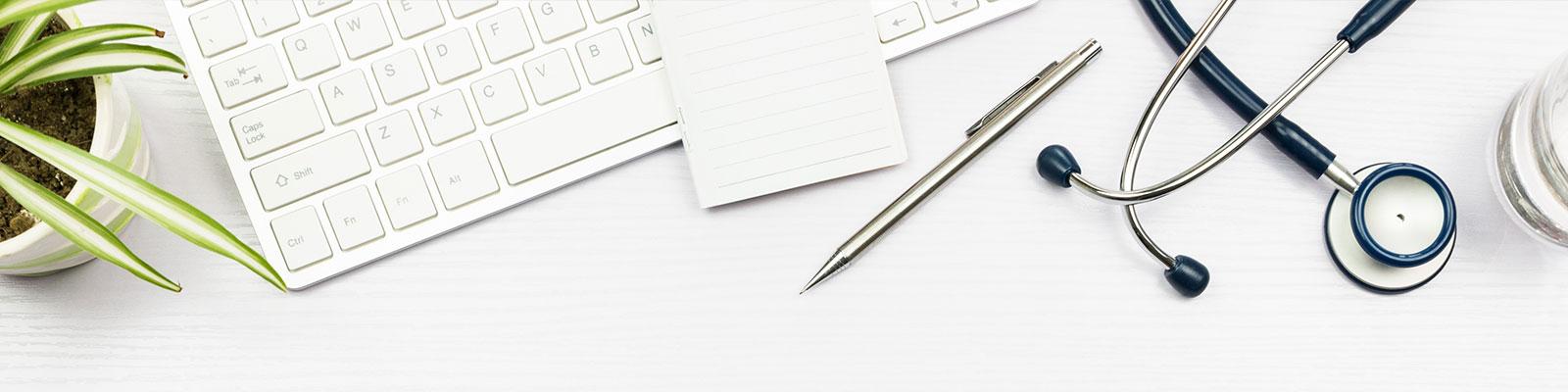 desktop with plant, computer keyboard, stethoscope, pen