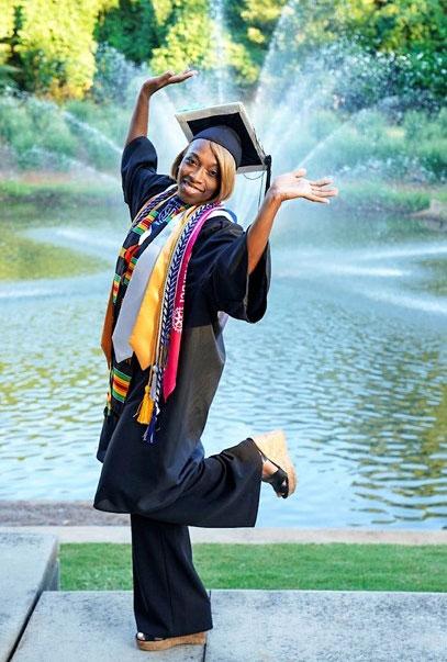 Female graduate posing in cap and gown in front of fountain