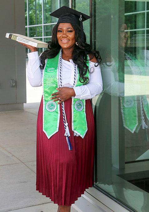 Female graduate with textbook posing in front of library