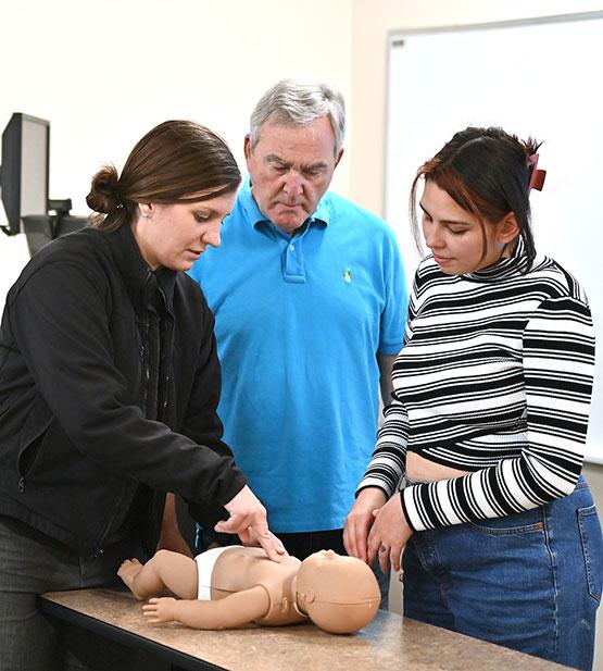 Dr. Kenneth Horowitz, assistant professor of physical education at GGC, and Allison Gonzalez watch as Ashley Still, GGC's emergency management coordinator, demonstrates chest compressions on a baby CPR mannequin.