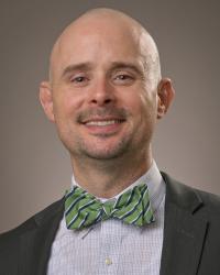 Dr. Matthew Robison wearing a black jacket, white shirt and green bowtie smiling at the camera