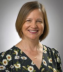 Dr. Christine Miller Divine wearing a black blouse with color flowers and smiling at the camera