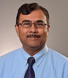 Dr. Atul Saxena wearing a blue dress shirt and tie, wearing glasses and smiling at camera