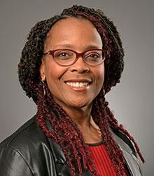 Dr. Alvina Atkinson wearing a black jacket, red shirt, brown-rimmed glasses and black smiling at the camera