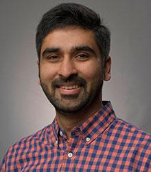 Dr. Umar Mujahid Khokhar wearing a checkered colored shirt and smiling at camera