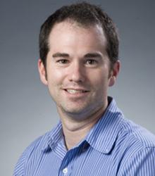Dr. Thomas Lilly wearing a light blue shirt and smiling at camera
