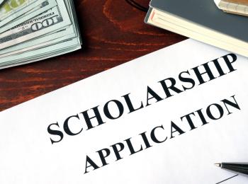 White paper with scholarship application written at the top, a stack of money and two notebooks