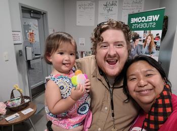 Travis and Anna Mendoza pose in a GGC office with their toddler daughter