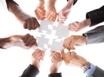 Multiple diverse hands hold pieces of a paper puzzle