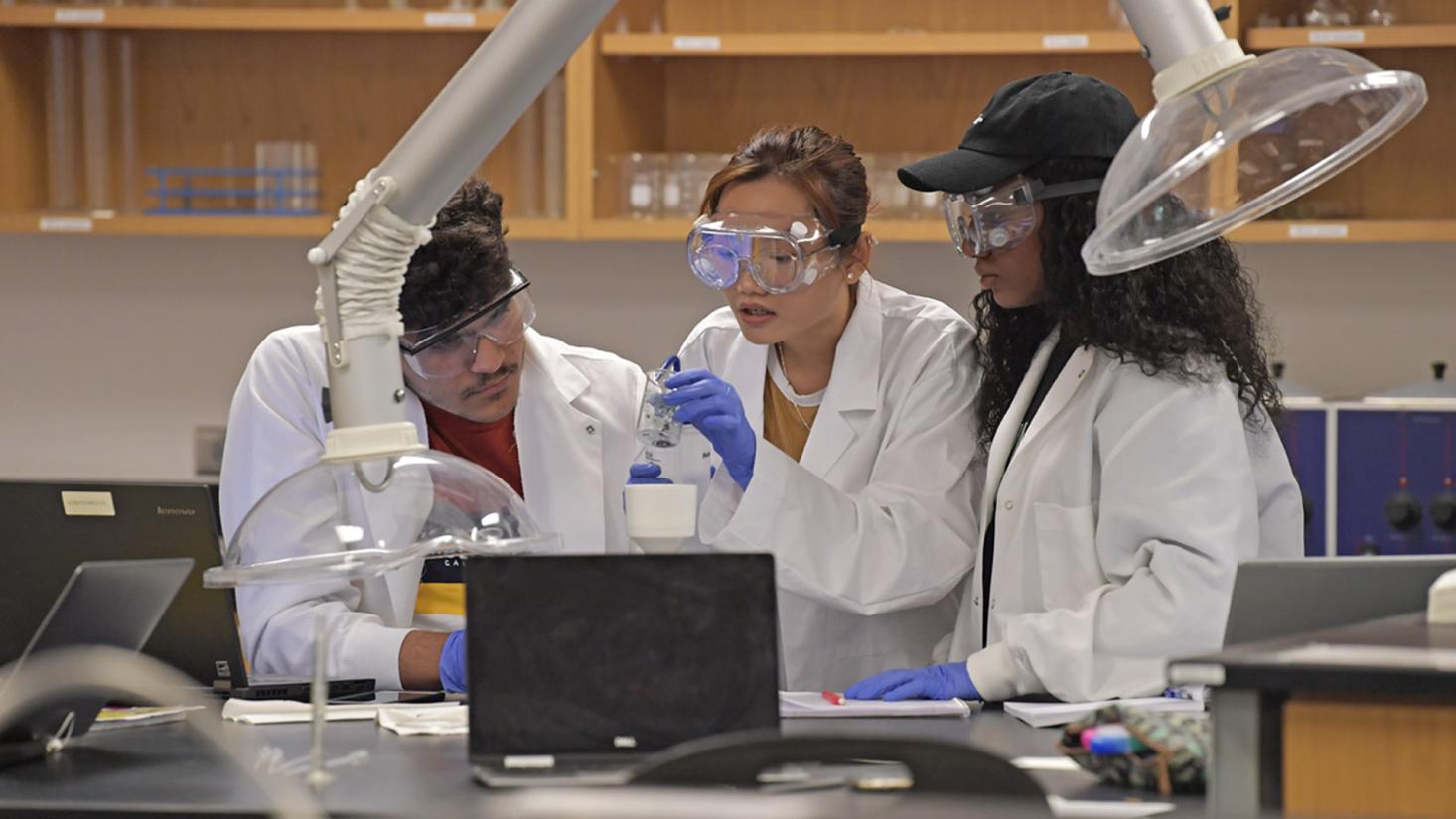 Three students looking at a beaker in class