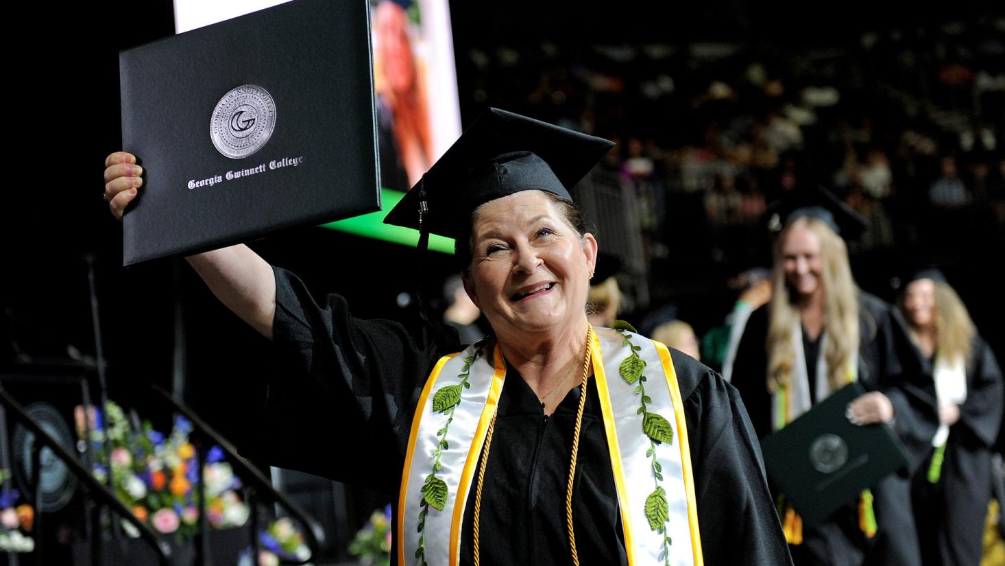 Woman holding up degree at graduation ceremony