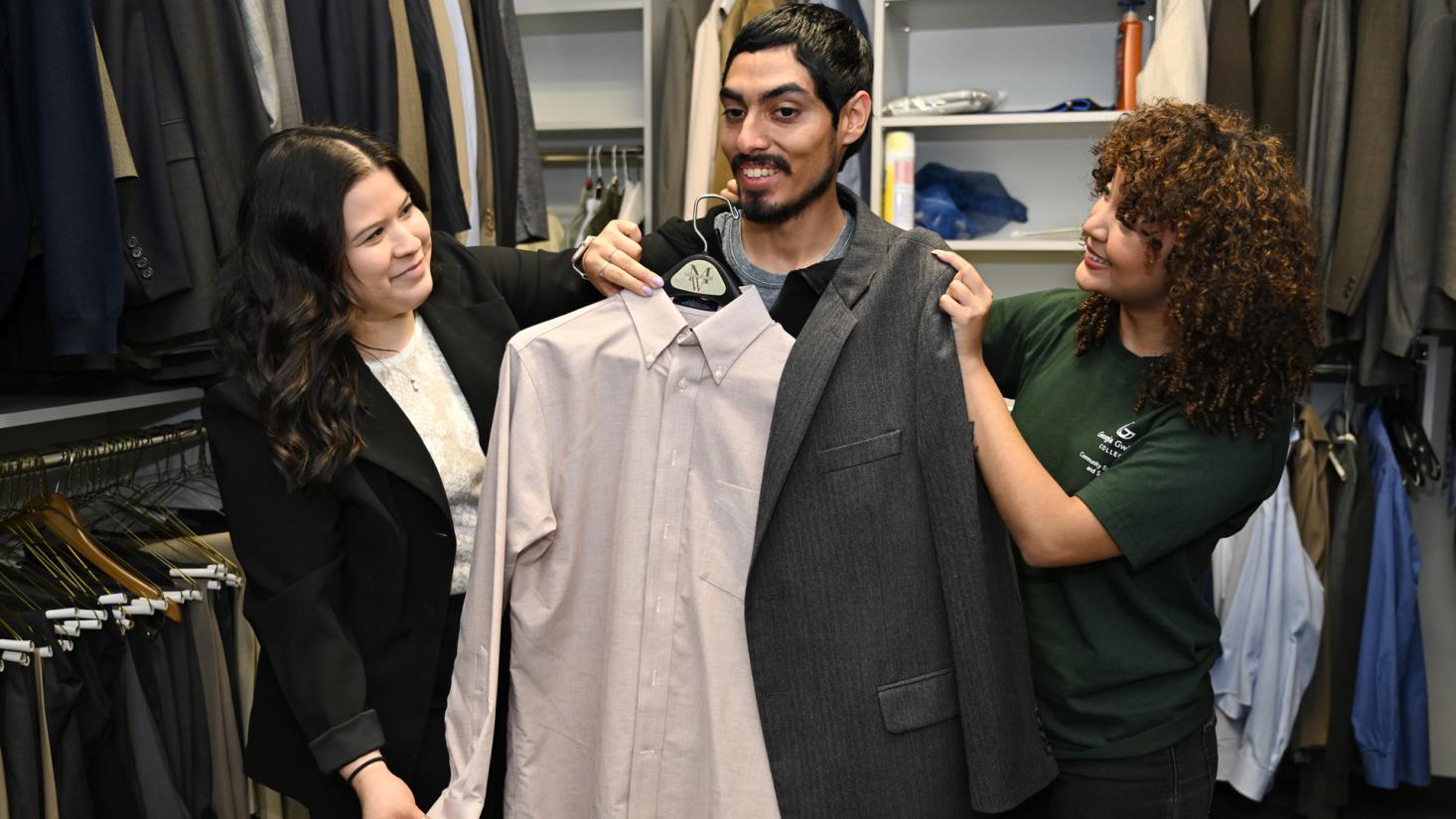 Two female students helping a male student choose clothing